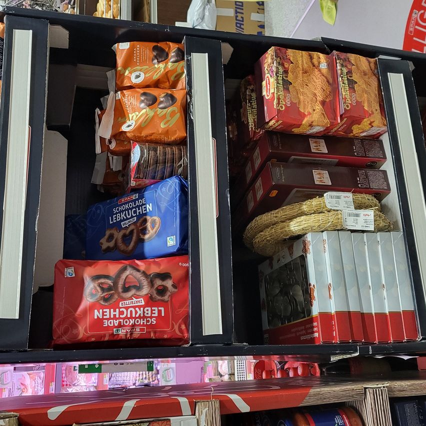 A shelf displaying assorted food products including chocolates, pretzels, and pasta with a white rope in the middle section.