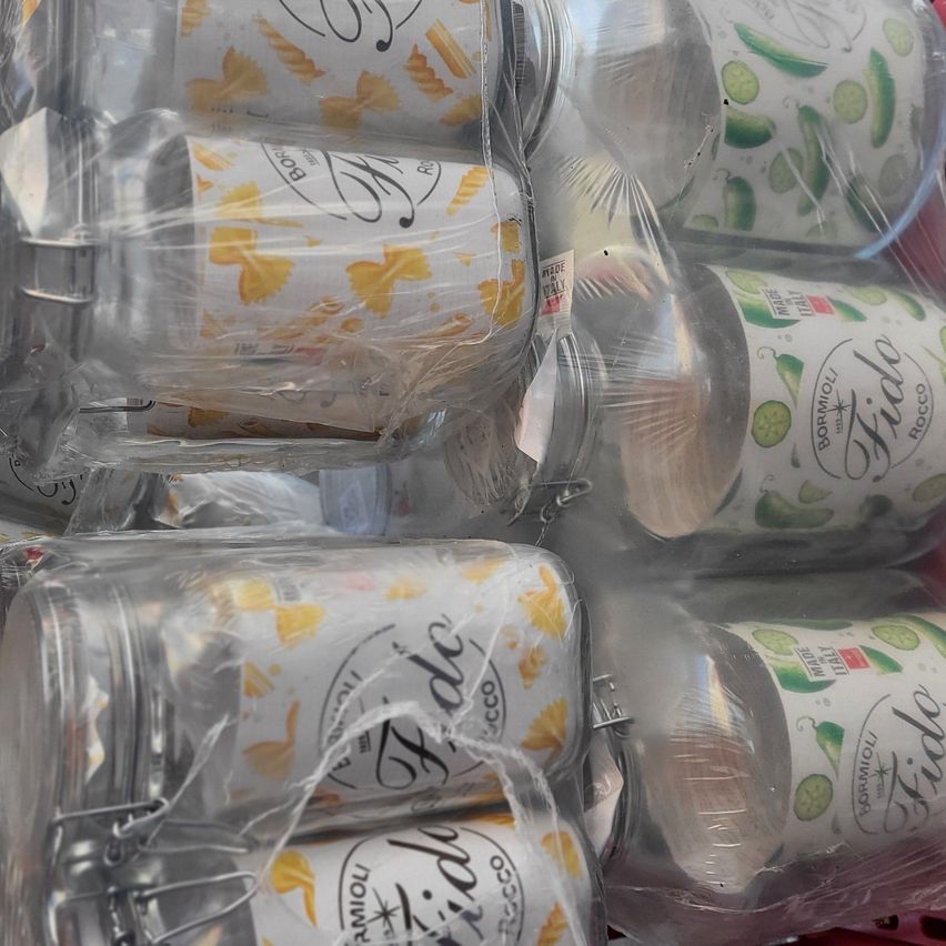 Several glass jars are wrapped in plastic, with two different designs: one with yellow shapes resembling pasta and the other with green limes and red chilies.