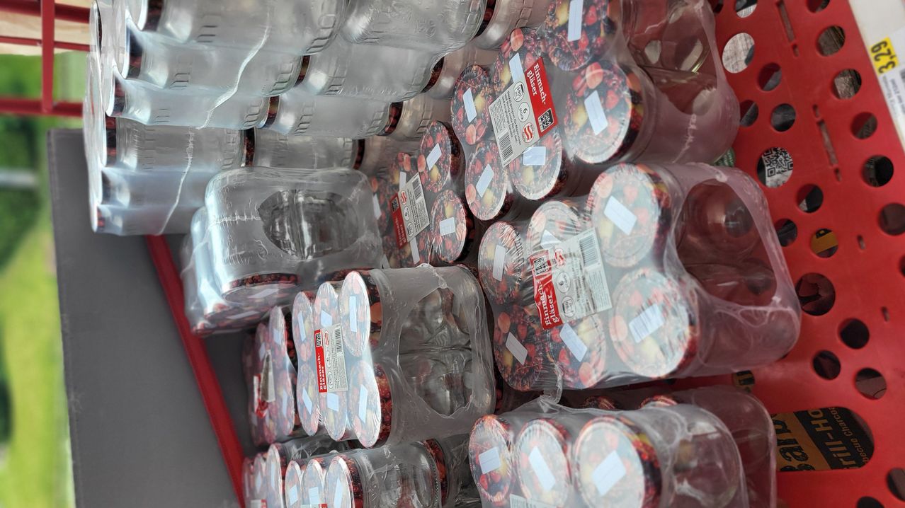 A close-up view of a stack of clear plastic containers filled with red fruits. Each container has a label with text and numbers, and is packed in a transparent plastic bag.
