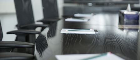 Ein leerer Besprechungsraum mit einem langen Holztisch und schwarzen Stühlen. Einige Notizblöcke und Bleistifte liegen auf dem Tisch.