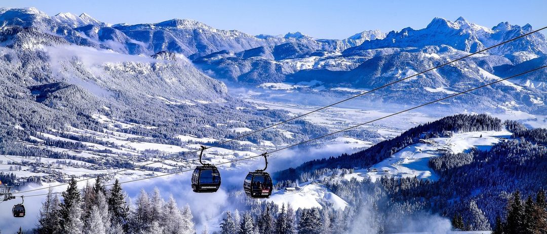 Eine Seilbahn fährt auf einem verschneiten Berg mit schneebedeckten Bäumen. Der Berg hat einen klaren blauen Himmel.