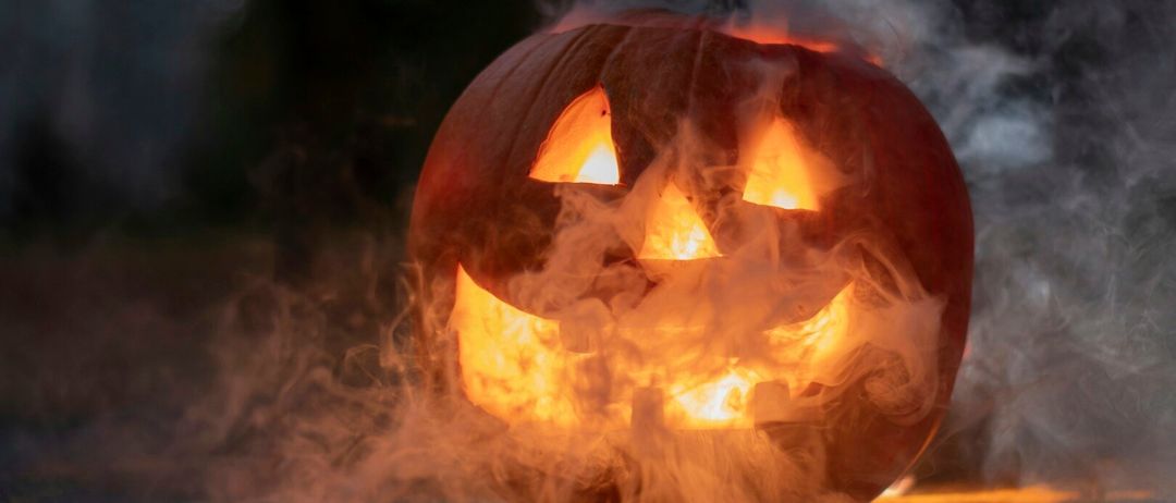 Ein gefertigter Kürbis mit einer brennenden Kerze im Inneren ist von Rauch umgeben in einem dunklen Bereich.
