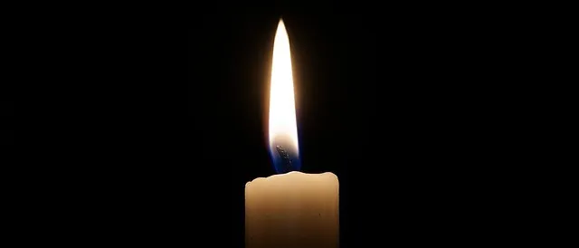 Eine brennende Kerze steht in einem dunklen Raum. Die Kerze ist weiß mit einer blauen Flamme. Die Flamme ist hell und erhellt die Kerze.