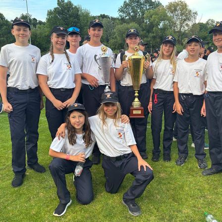 Eine Gruppe junger Menschen in passenden Uniformen posiert mit Trophäen auf einem Rasenfeld. Sie haben lächelnde Gesichter.