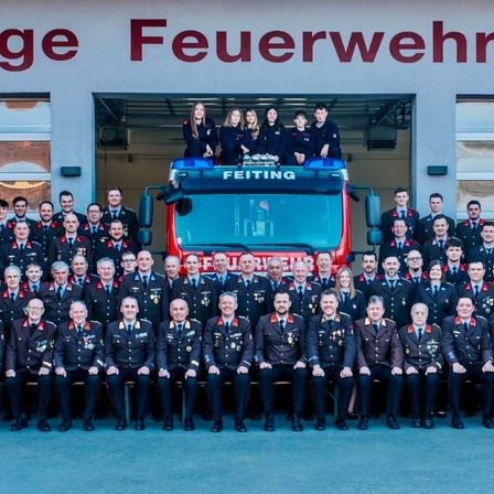 Eine Gruppe Feuerwehrleute in Uniform, mit einer Frau auf dem Feuerwehrwagen, posiert für ein Foto.