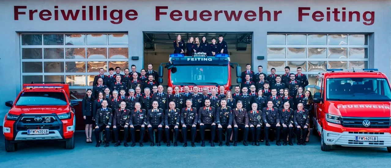 Eine Gruppe Feuerwehrleute in Uniform, mit einer Frau auf dem Feuerwehrwagen, posiert für ein Foto.