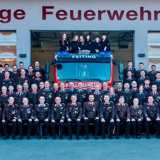 Eine Gruppe Feuerwehrleute in Uniform, mit einer Frau auf dem Feuerwehrwagen, posiert für ein Foto.