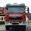 Freiwillige Feuerwehr Feiting-Logo. Ein roter Feuerwehrwagen mit 'Feuerwehr' und 'Feiting' auf der Front. Er hat Kränze und ein Nummernschild LB 851 FF. Dahinter steht ein Haus mit Zaun und Bäumen.