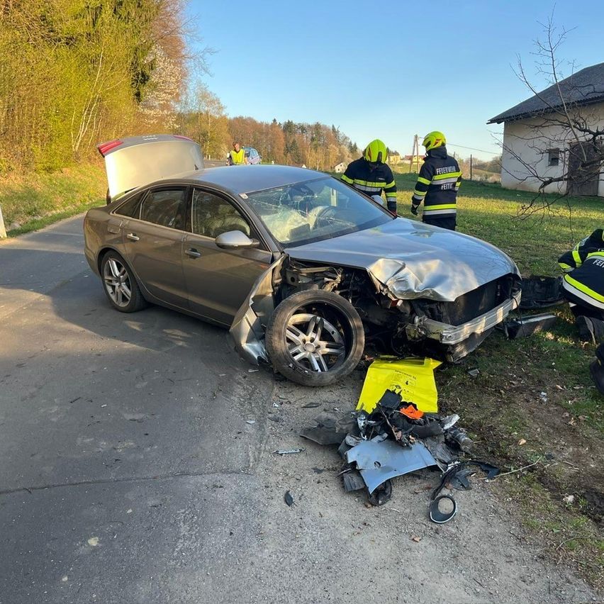 Ein beschädigtes Auto ist am Straßenrand geparkt. Rettungskräfte stehen dahinter.