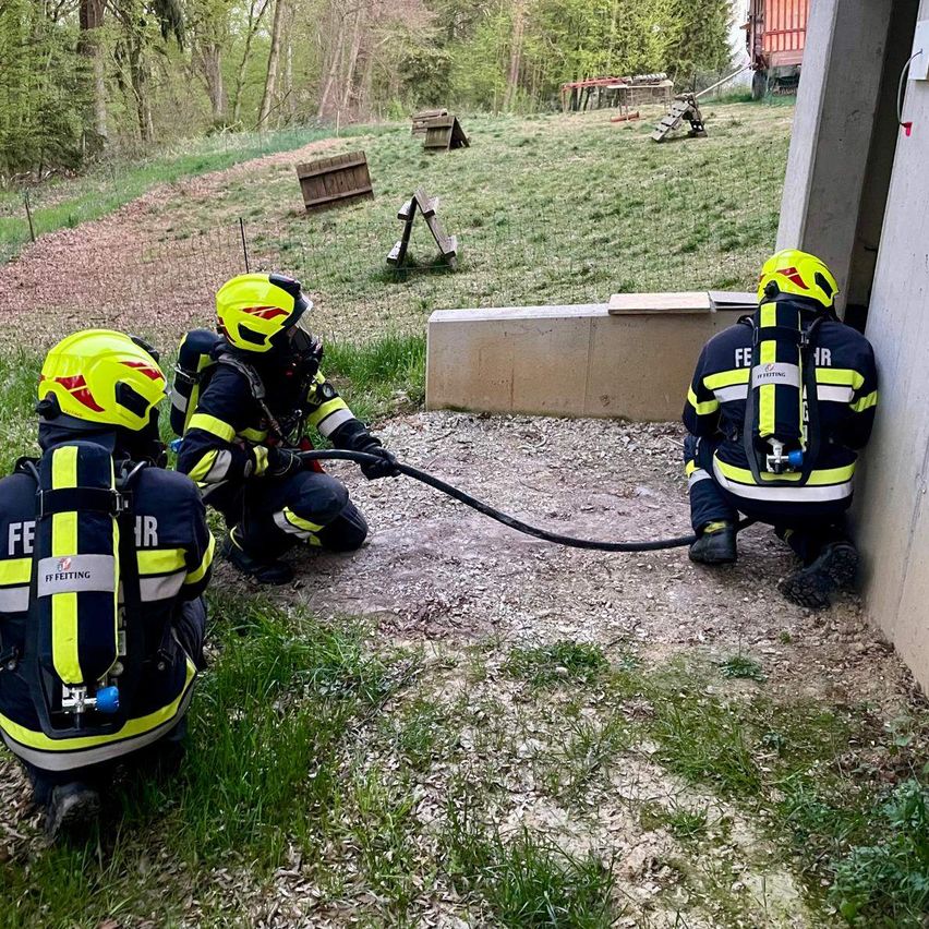 Vier Feuerwehrleute in voller Ausrüstung üben am Fuße eines Gebäudes mit einer angeschlossenen Wasserleitung.