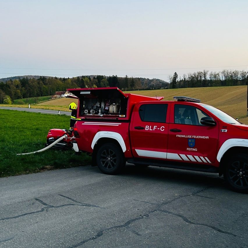 Ein roter Feuerwehrwagen mit BLF-C an der Seite ist auf einer Straße geparkt. Eine Person steht neben dem Wagen. Ein Schlauch ist angeschlossen.