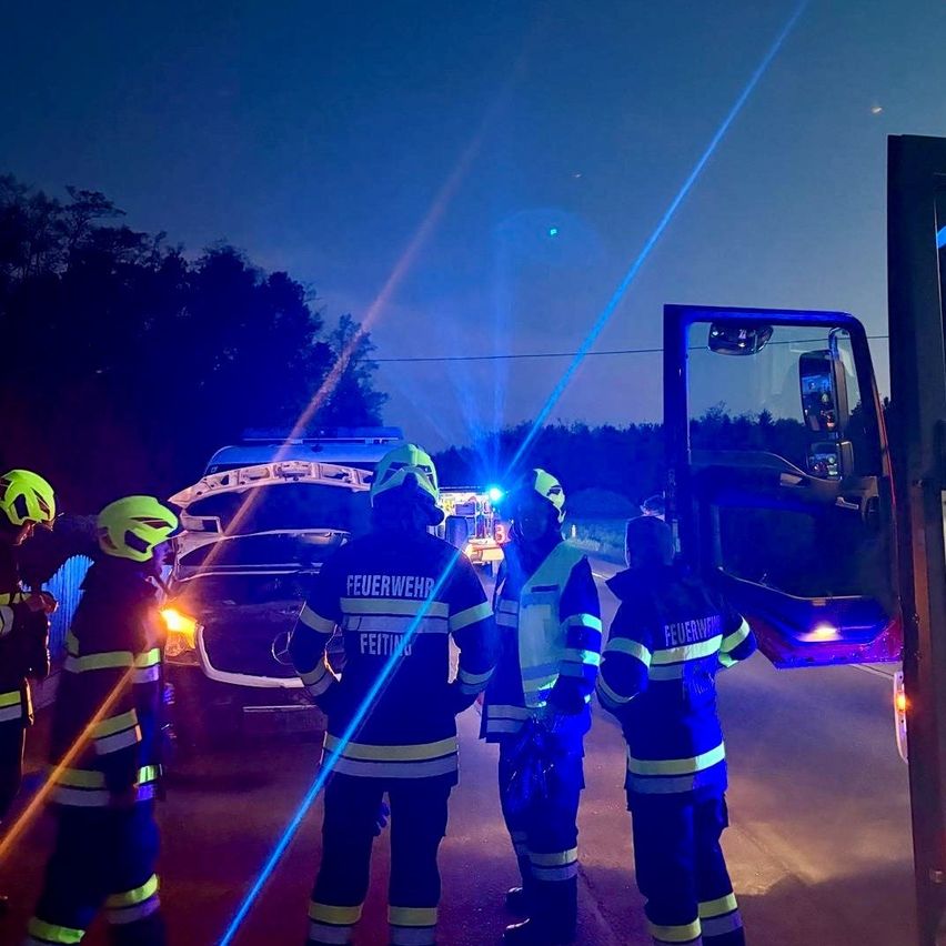 In der Nacht stehen Feuerwehrleute in der Nähe eines Autos mit offenem Motorhaube, einer hält eine Taschenlampe und der andere eine Taschenlampe.