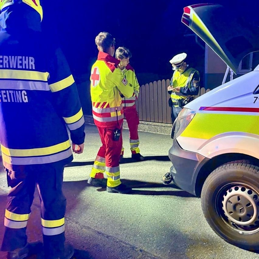 Rettungskräfte stehen bei Nacht neben einer geöffneten Autohaube. Eine Person in Uniform schreibt auf Papier.
