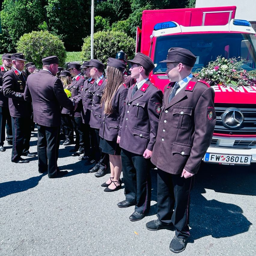 Eine Gruppe Feuerwehrleute in Uniform steht in einer Reihe vor einem roten Feuerwehrauto mit Blumen.