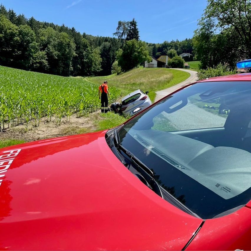 Ein roter Feuerwehrwagen und ein umgekipptes Auto neben einem Maisfeld. Eine Person in Orange überprüft das Auto, während eine andere kniet.