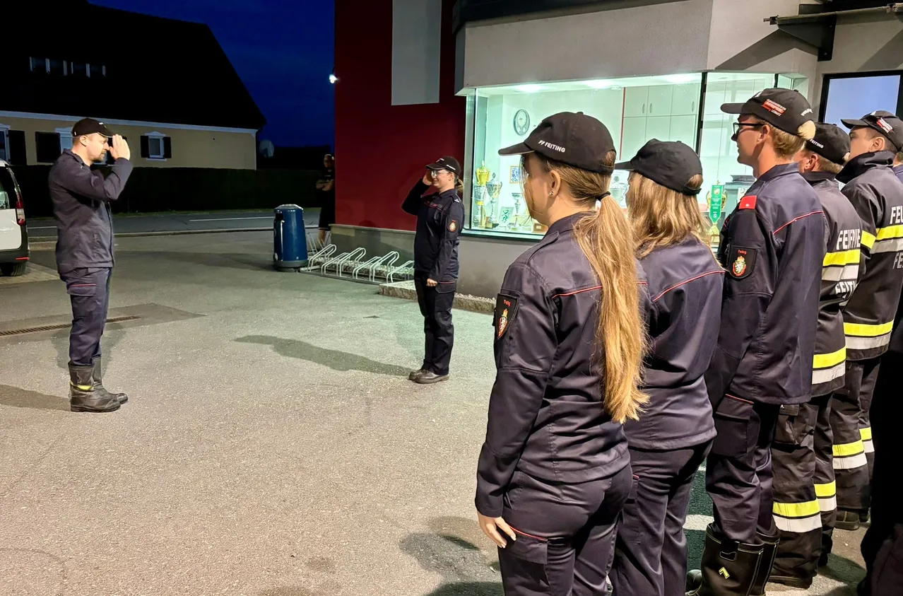 Eine Gruppe von Feuerwehrleuten in Uniform steht nachts vor einem Gebäude.