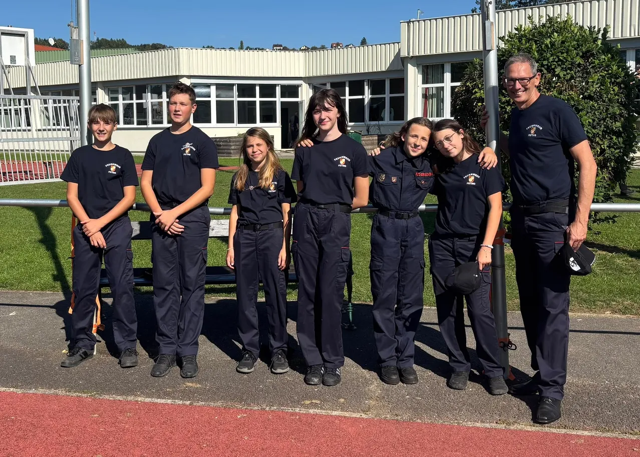 Eine Gruppe junger Menschen in dunkelblauen Uniformen steht vor einem Gebäude.