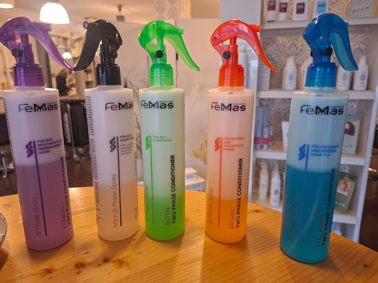 Fünf Sprühflaschen mit Haarpflegeprodukten, darunter Zweiphasen-Conditioner und andere Marken, stehen auf einem Holztisch. Die Flaschen sind in verschiedenen Farben und Größen.