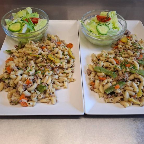 Zwei weiße Teller mit Nudeln und Gemüse, einer mit einer Salatschüssel links und der andere rechts.