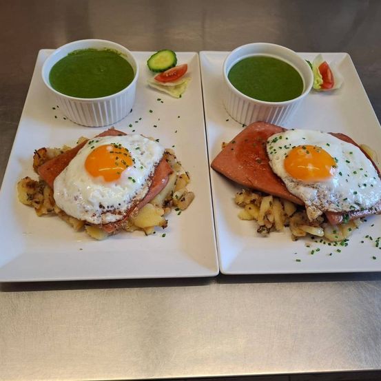 Zwei Teller mit Räucherlachs, gebratenen Eiern und grüner Sauce auf einer Metalloberfläche.