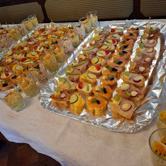 Ein Tisch mit verschiedenen Vorspeisen auf Silberfolientabletts, einschließlich Sandwiches mit Gemüse und Früchten und kleinen Tassen mit Dips.
