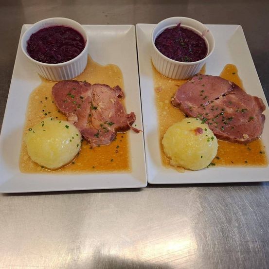 Zwei Teller eines traditionellen deutschen Gerichts mit Roastbeef, Kartoffelpüree und Rotkohl, serviert auf einer Edelstahloberfläche.