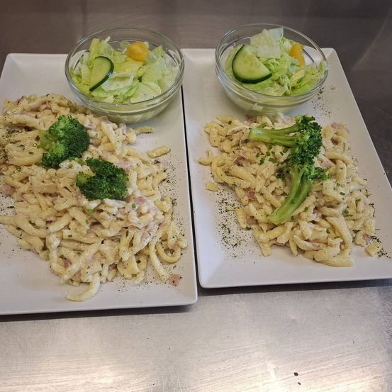 Zwei weiße Teller mit Nudeln, Brokkoli und Salat in einer Schüssel. Die Nudeln sind cremig mit Schinken und Käse.