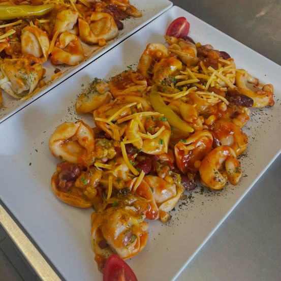Zwei weiße Teller mit Nudeln, überzogen mit Tomatensauce, Bohnen, Käse und mit grünen Kräutern und einer Tomatenscheibe garniert.