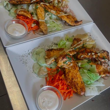 Zwei Teller mit gegrilltem Hähnchen, Salat, Karotten und Bohnen. Jeder Teller hat eine kleine Schüssel Dressing.
