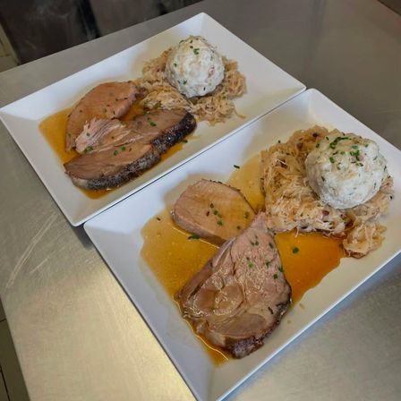 Zwei Teller mit gebratenem Fleisch, Sauerkraut und einer Kartoffelknödel auf einer Metalloberfläche.