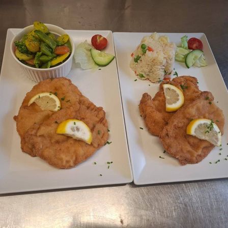 Zwei Teller mit paniertem gebratenem Hähnchen mit Zitronenscheiben, einer mit einer Beilage aus gemischtem Gemüse und Reis.