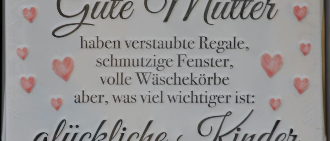Ein Schild zeigt den Text 'Gute Mitte haben verstaubte Regale, schmutzige Fenster, volle Waschekorbe aber, was viel wichtiger ist: Knickliche Kinde.' Das Bild ist ein Nahaufnahme.