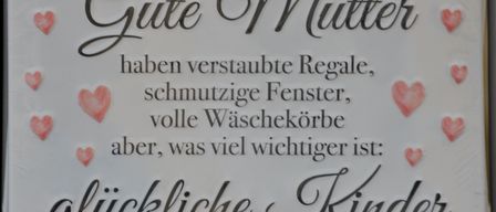 Ein Schild zeigt den Text 'Gute Mitte haben verstaubte Regale, schmutzige Fenster, volle Waschekorbe aber, was viel wichtiger ist: Knickliche Kinde.' Das Bild ist ein Nahaufnahme.