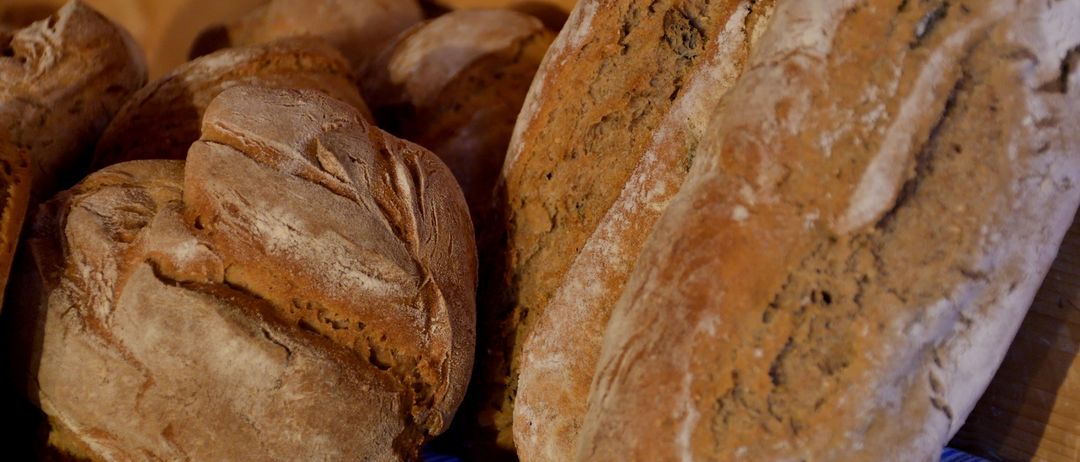 Ein Nahaufnahme von mehreren Lagen braunen Brots, mit einer leichten Bestäubung von Mehl auf einigen von ihnen, ist auf einer Holzoberfläche angeordnet.