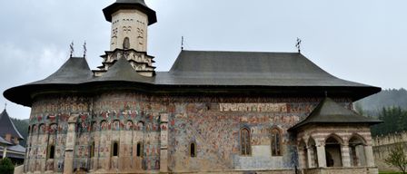 Ein Paar geht mit einem Schirm vor einer historischen Kirche mit einem Kirchturm und detaillierten Wandgemälden.