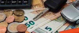 Ein Taschenrechner, Autoschlüssel, ein Spielzeugauto, Münzen und Scheine liegen auf einem Holztisch.