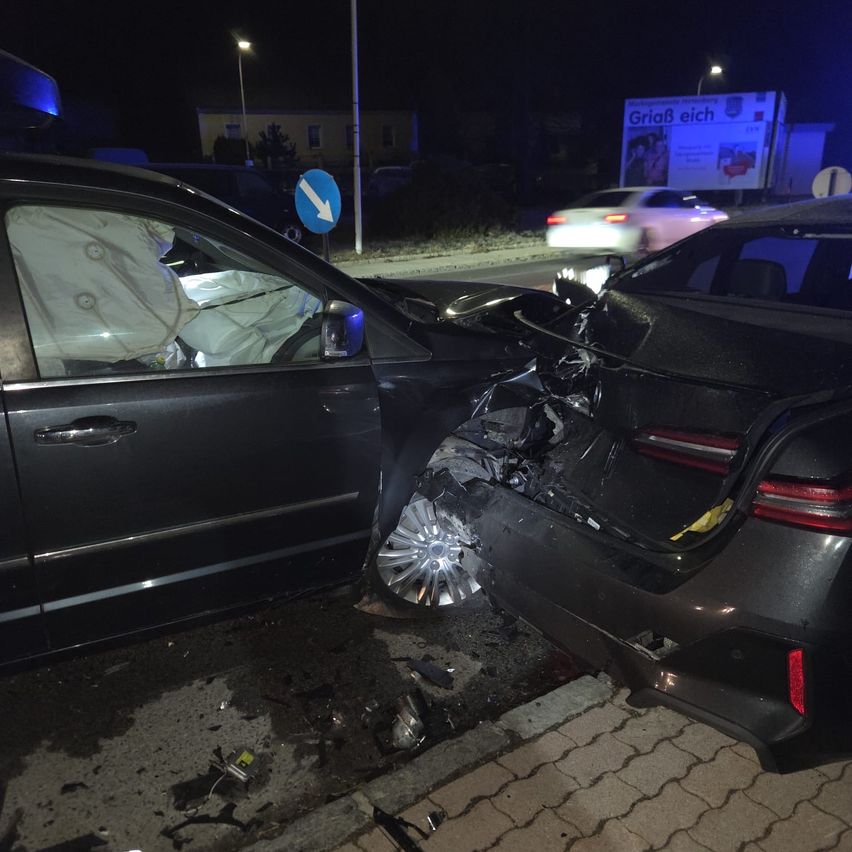 Zwei schwarze Autos sind nachts auf einer asphaltierten Straße schwer beschädigt, mit ausgelösten Airbags und verstreuten Trümmern.