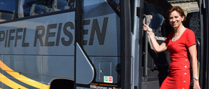 Eine Person in einem roten Shirt hält den Türgriff eines Busses. Das Wort REISE ist an der Seite des Busses angebracht.