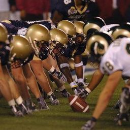 Ein Football-Team in Helmen und Handschuhen steht auf dem Feld. Die Spieler sind bereit für einen Snap. Die Nummer 8 ist auf dem Trikot eines Spielers zu sehen.