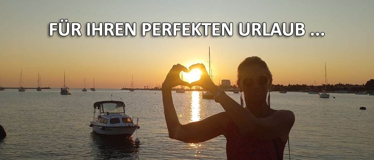 Eine Frau steht auf einem Steg und formt mit ihren Händen ein Herz bei Sonnenuntergang. Im Hintergrund segeln Boote auf dem Wasser.