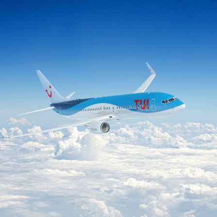 Ein blaues und weißes Flugzeug mit dem Wort 'TUIfly' auf der Seite fliegt in der Luft über den Wolken.