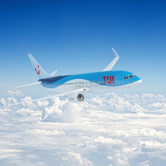 Ein blaues und weißes Flugzeug mit dem Wort 'TUIfly' auf der Seite fliegt in der Luft über den Wolken.