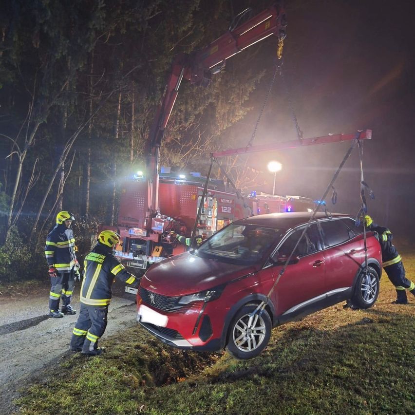 Feuerwehrleute heben einen roten SUV bei Nacht mit einem Kran hoch.