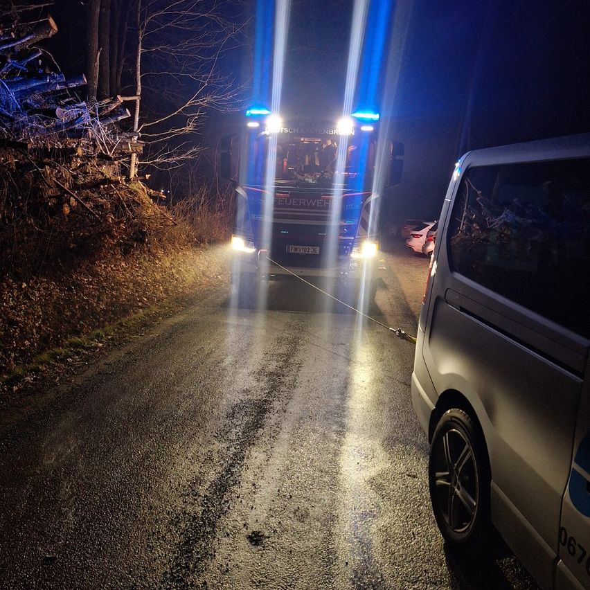 Ein Feuerwehrauto mit blauen Lichtern steht bei Nacht auf einer Straße. Ein Van ist neben dem Feuerwehrauto geparkt. Ein Auto steht am Straßenrand.