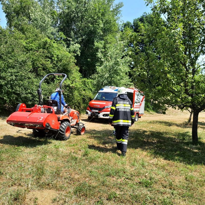Ein Feuerwehrmann geht auf einen roten Traktor zu, auf dem ein Mann sitzt. Ein Krankenwagen steht hinter dem Traktor.