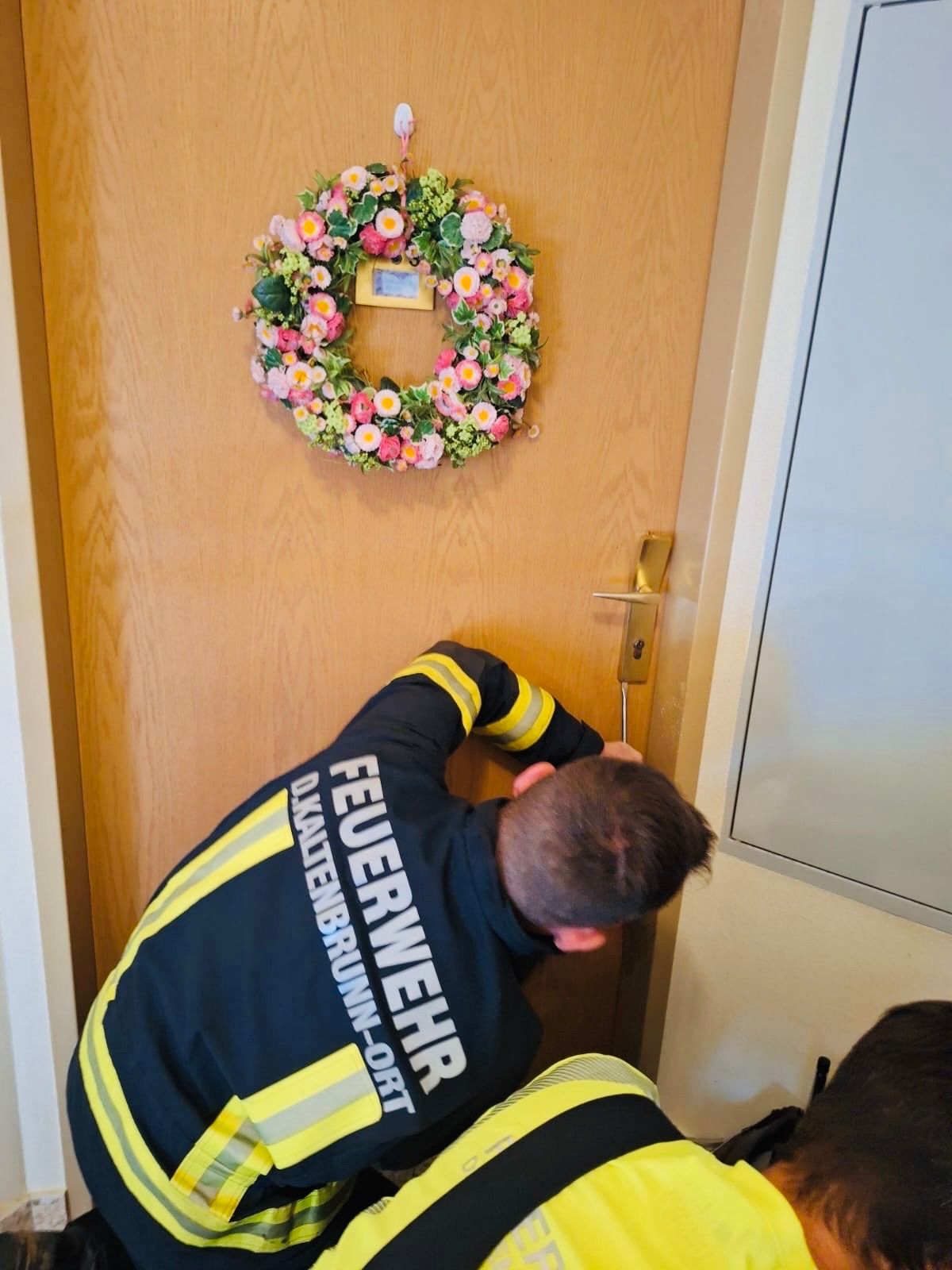 Feuerwehrmann von der FF-Kaltenbrunn-Ort öffnet eine Tür mit einem Werkzeug, Tür mit Blumenkranz