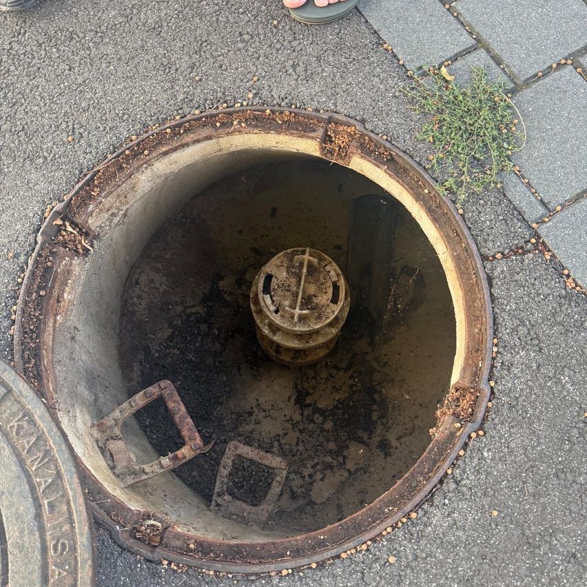 Kanaldeckel mit offenem Schacht und Einbauten in einem Stadtgebiet.