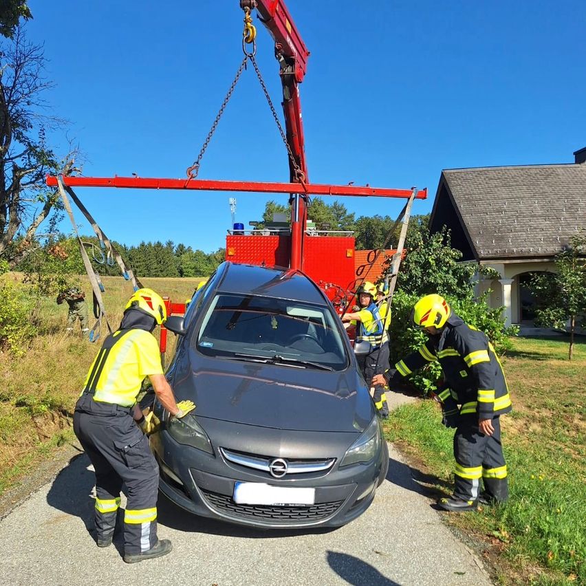 Eine Gruppe von Feuerwehrleuten benutzt einen Kran, um ein Auto vom Boden zu heben. Sie tragen gelbe Helme und Schutzanzüge.