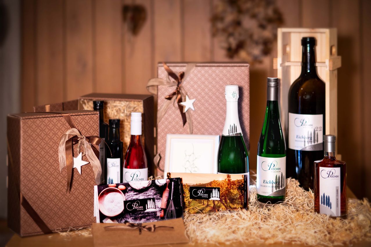 Verschiedene Weinflaschen, einschließlich eines Champagners, sind auf einem Tisch mit einem hölzernen Hintergrund angeordnet, begleitet von Geschenkboxen und einem dekorativen Stern.