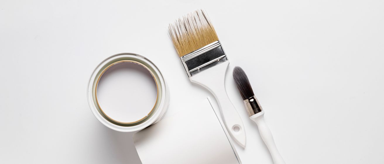 Eine Farbdose, ein Farbroller und ein Pinsel liegen auf einer weißen Oberfläche. Die Farbdose ist geöffnet, mit weißer Farbe im Inneren. Der Farbroller hat einen weißen Griff und einen schwarz-weißen Pinsel. Der Pinsel hat einen weißen Griff und einen schwarz-weißen Pinsel.